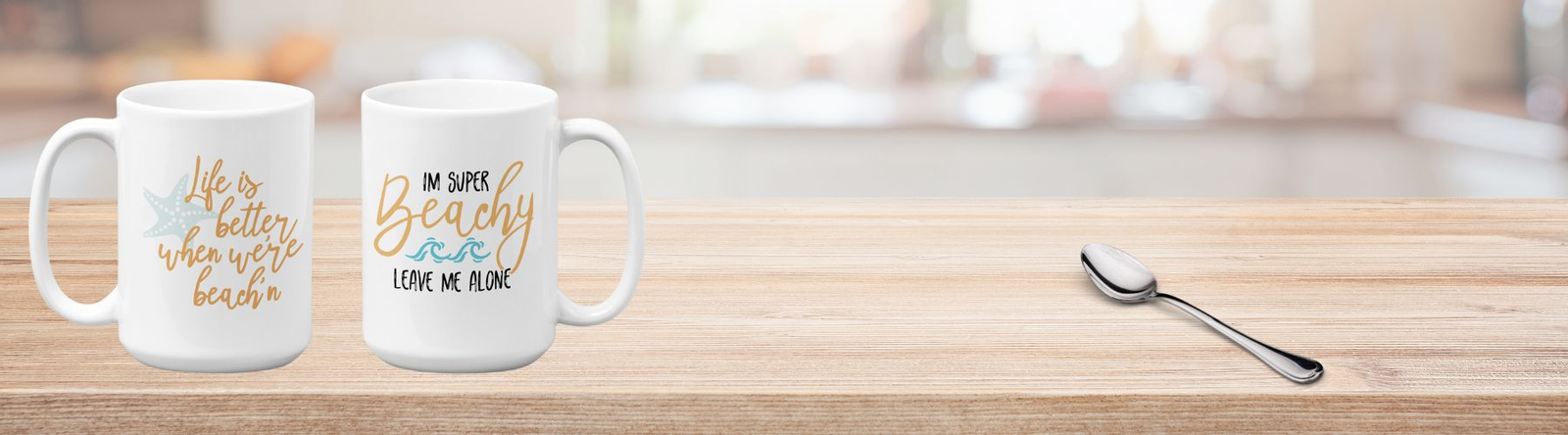 Beach Coffee Mugs show two white mugs and a spoon on a kitchen counter made of butcher block. One mug says Leave Me Alone, I'm Feeling Super Beachy. The other says Life Is Better When We're Beachin'.